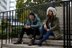 Mann und Frau sitzen auf einer Treppe mit Outdoor-Parkas 