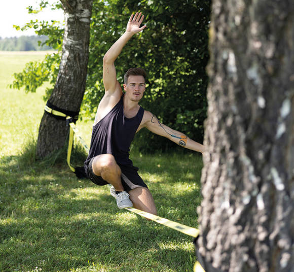 Mann balanciert auf einer Slackline zwischen zwei Bäumen 