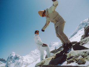 Skiers wearing beige and white explore rock terrain with mountains in the background.