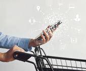 Frau mit Einkaufswagen und Smartphone inklusive Multichannel-Icons