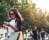 Junge Frau beim Einkaufen schaut auf ihr Handy