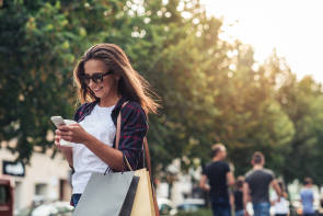 Junge Frau beim Einkaufen schaut auf ihr Handy 