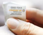 Hand hält Oeko-Tex-Schild an Textilien