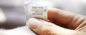Hand hält Oeko-Tex-Schild an Textilien 