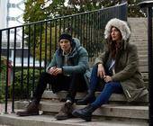 Mann und Frau sitzen auf einer Treppe mit Outdoor-Parkas