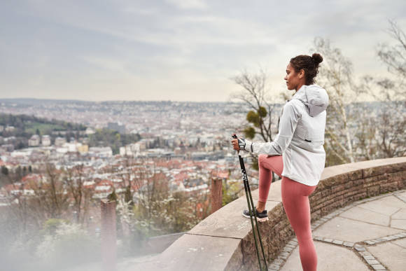 Frau mit Nordic-Walking-Stöcken schaut auf Stadt hinab 