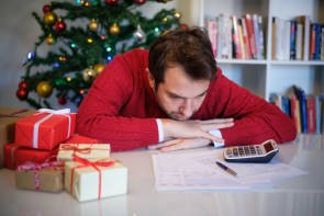 Mann grübelt vor dem Weihnachtsbaum über Rechnungen 
