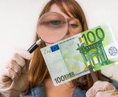 Frau schaut mit Lupe Hundert-Euro-Schein an