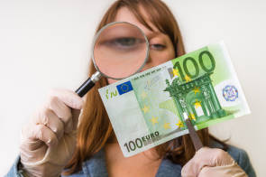 Frau schaut mit Lupe Hundert-Euro-Schein an 