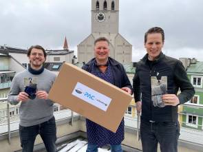 drei Männer mit P.A.C.-Paket über den Dächern Münchens 