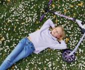 Kind liegt in Blumenwiese mit Scooter neben sich