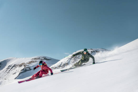 Zwei Skifahrer auf Piste mit blauem Himmel 