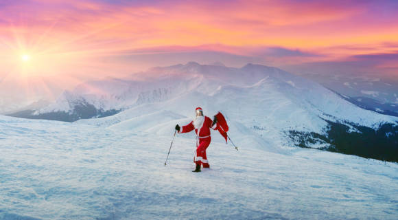 Weihnachtsmann mit Wanderstöcken im verschneiten Gebirge 