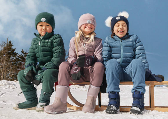 drei Kinder mit Winterbekleidung sitzen auf Schlitten 