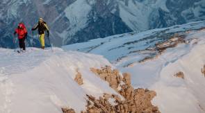 Zwei Skitourengeher bei Aufstieg vor Bergkulisse. 