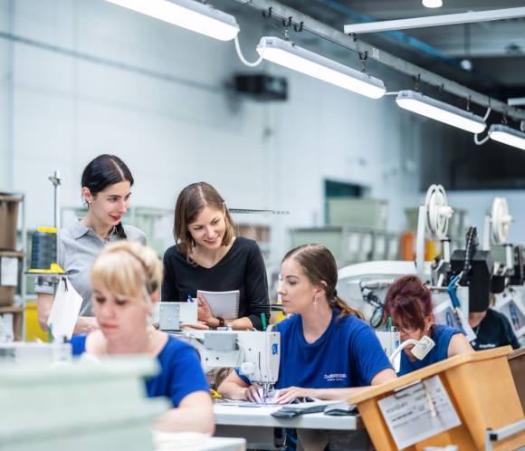 Veronika Becker (M.), Corporate Responsibility Managerin bei Lowa, spricht im Fertigungswerk des Schuhunterenhemnes in der Slowakei mit den Mitarbeiterinnen und Mitarbeitern. 